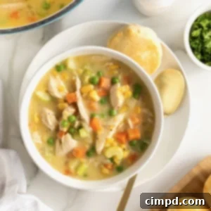 A crisp white ceramic bowl of creamy Chicken Pot Pie Soup on a white plate with a spoon, ready to be enjoyed.