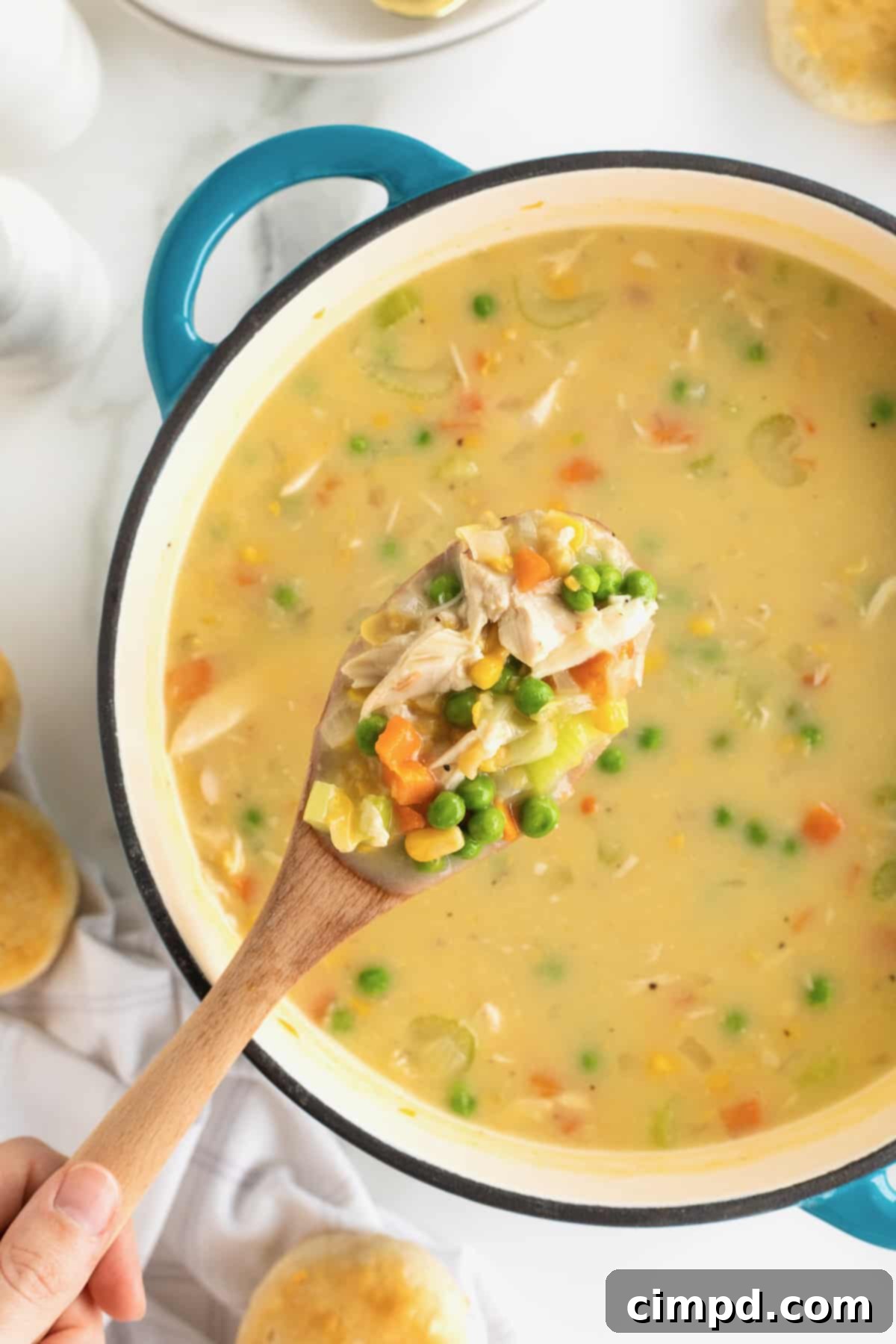 A vibrant blue Dutch oven, filled to the brim with creamy Chicken Pot Pie Soup, with a rustic wooden spoon invitingly emerging from the rich concoction.