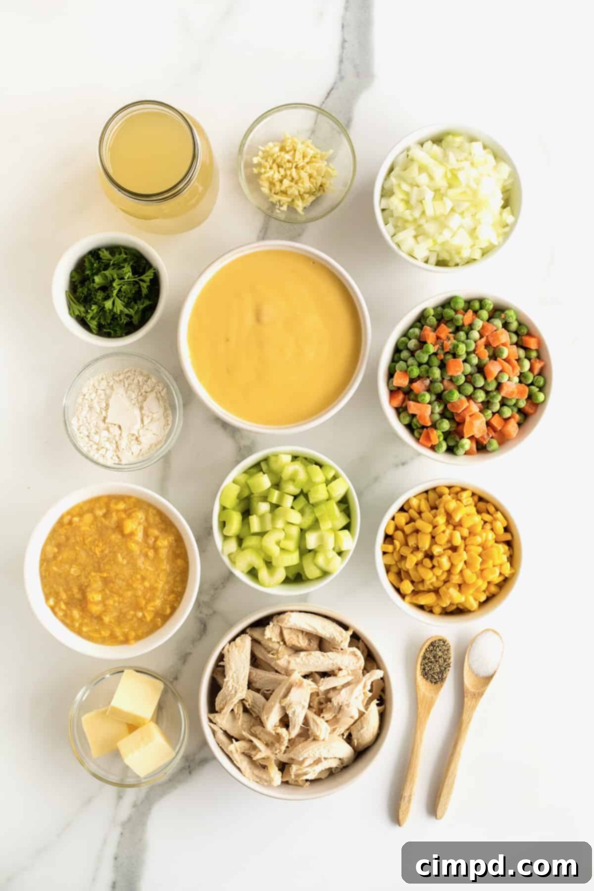 Various fresh and pantry ingredients for chicken pot pie soup, meticulously arranged in small white ceramic containers on a pristine white marble counter, ready for cooking.