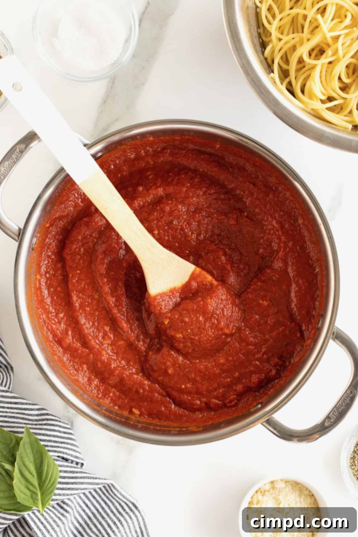 A large pot brimming with vibrant red homemade marinara sauce, featuring a white-handled wooden spoon resting inside.