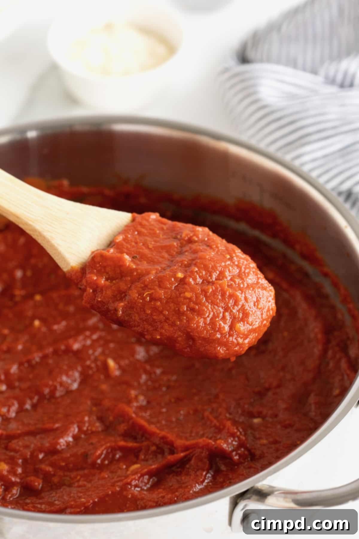 A large pot on the stove, filled with rich, red marinara sauce. A wooden spoon with a white handle rests inside, ready to stir.