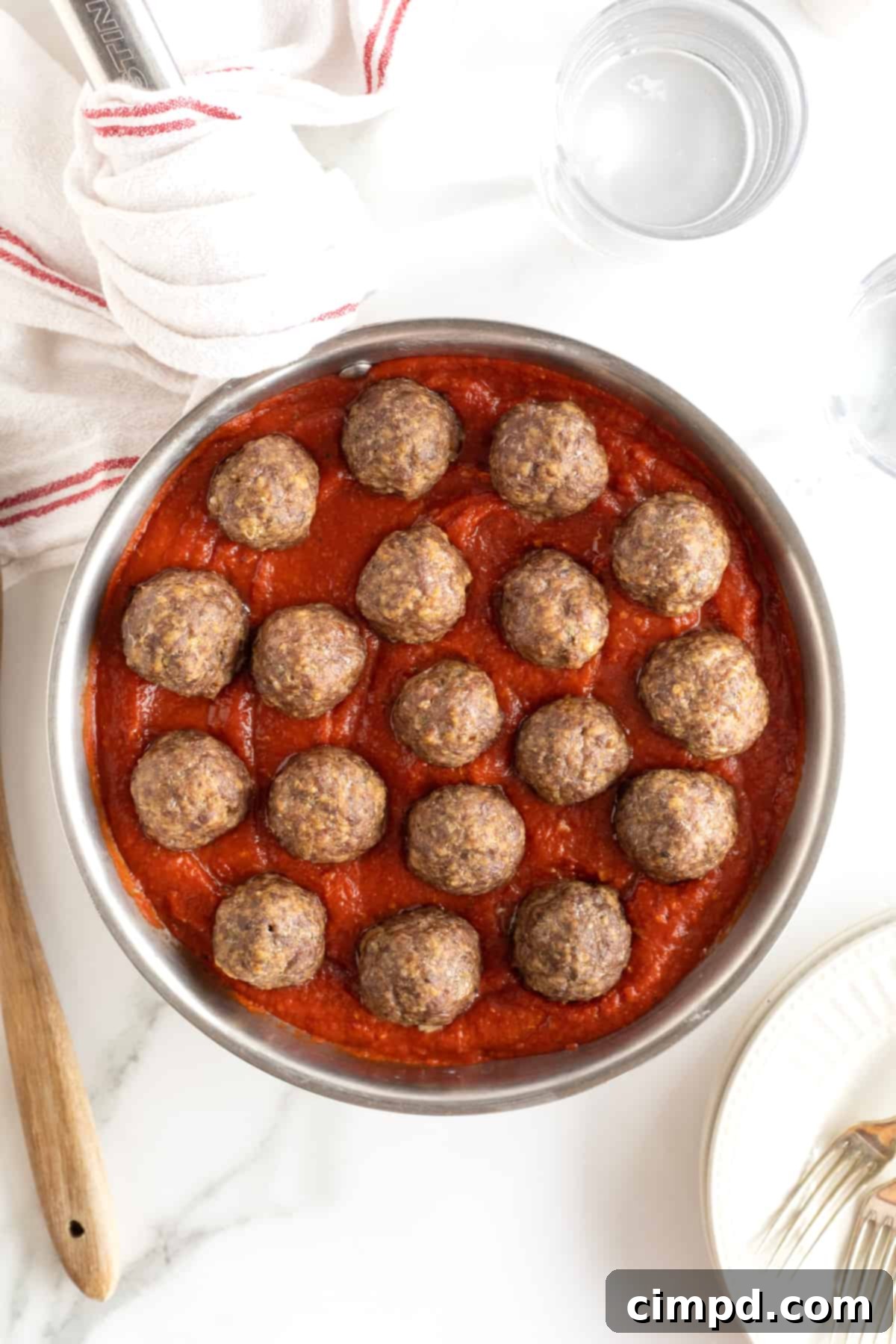 A round aluminum rimmed pan with filled with marinara sauce and meatballs arranged in a circle.