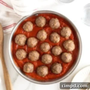 A round aluminum rimmed pan with filled with marinara sauce and meatballs arranged in a circle.