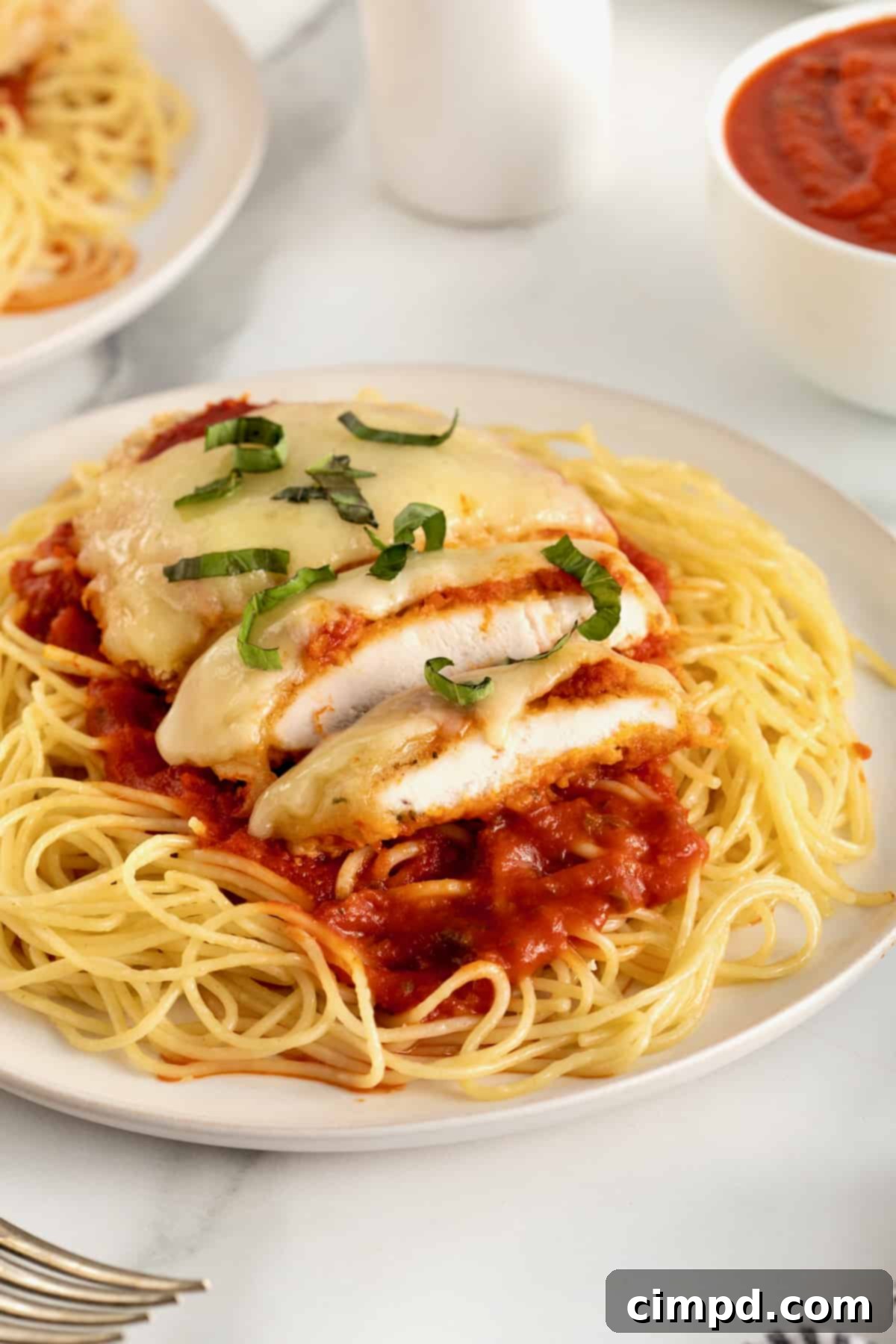 Chicken parmesan over marinara sauce and a bed of angel hair pasta on a white dinner plate.
