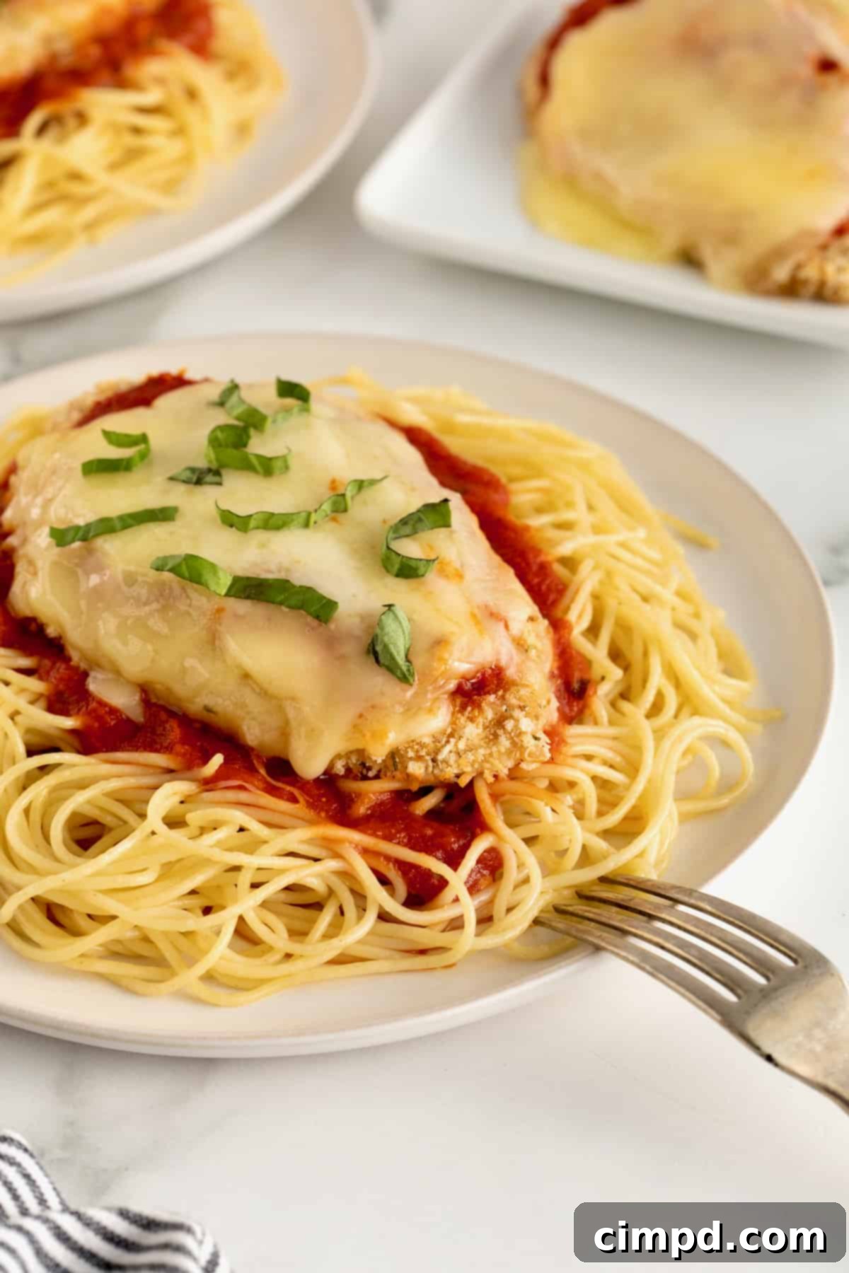 Chicken parmesan over marinara sauce and a bed of angel hair pasta on a white dinner plate.