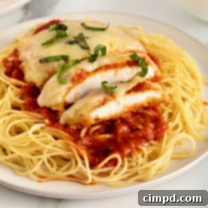 Chicken parmesan over marinara sauce and a bed of angel hair pasta on a white dinner plate.