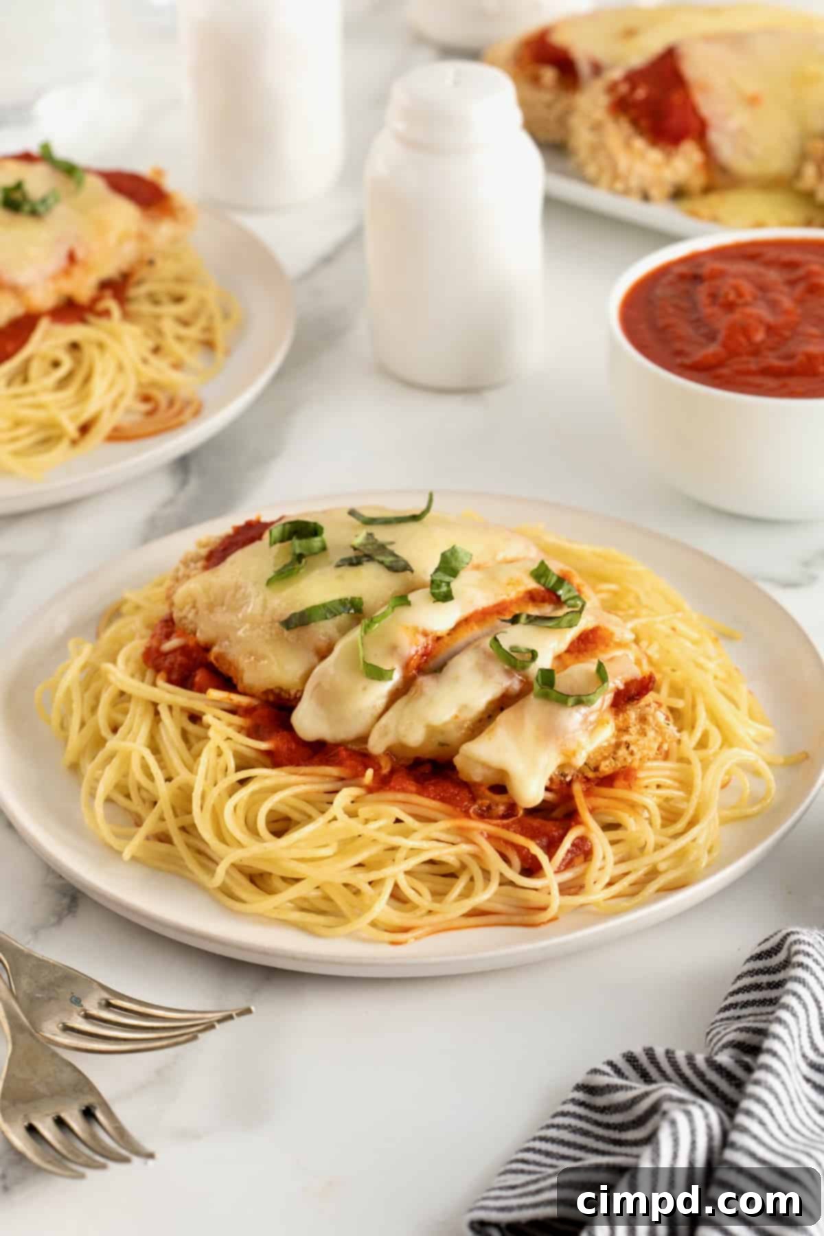 Chicken parmesan over marinara sauce and a bed of angel hair pasta on a white dinner plate.
