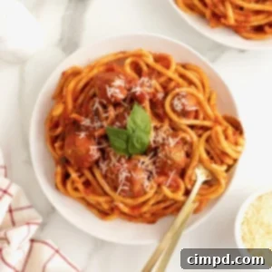 A large white plate with spaghetti and meatballs. The spaghetti is garnished with three fresh basil leaves.
