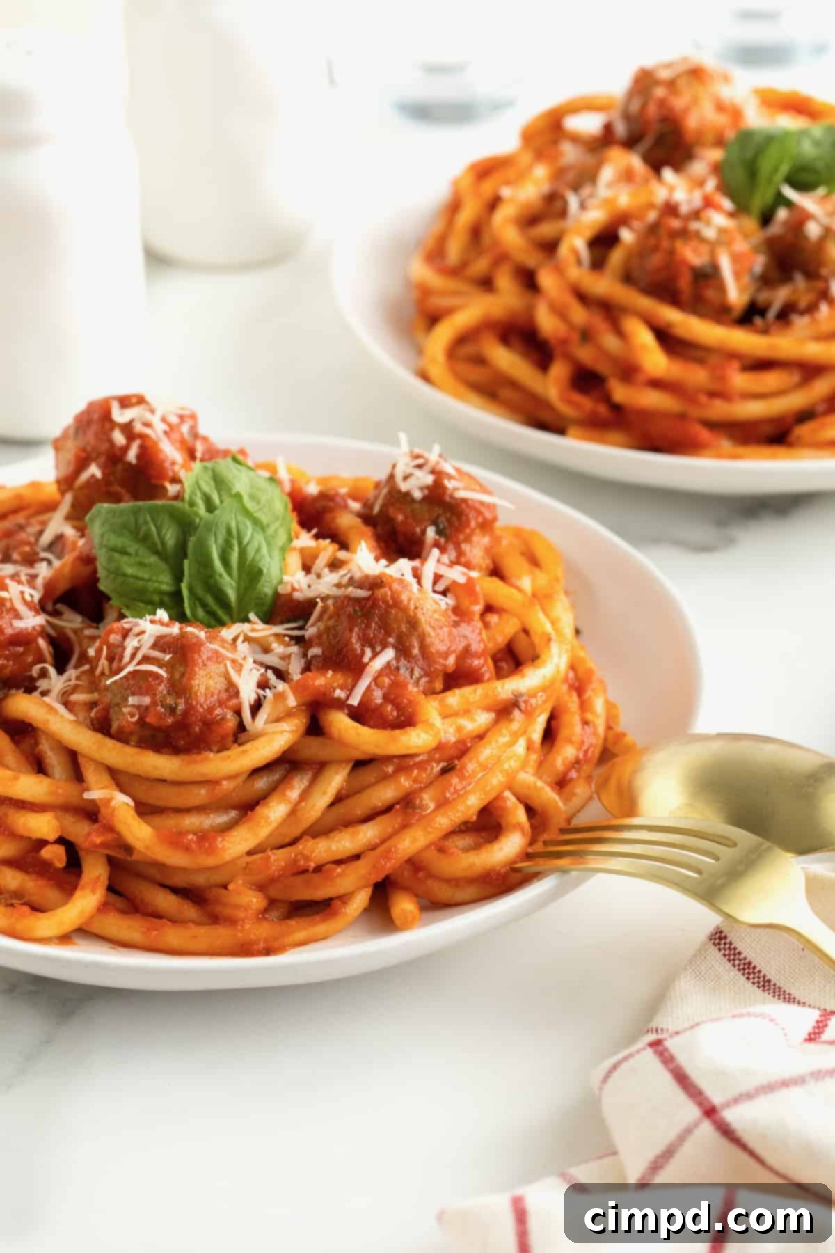 A large white plate with spaghetti and meatballs. The spaghetti is garnished with three fresh basil leaves.