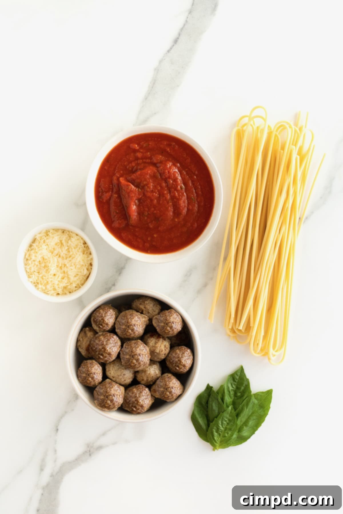 Ingredients for Spaghetti and meatballs in white dishes on a white marble counter.