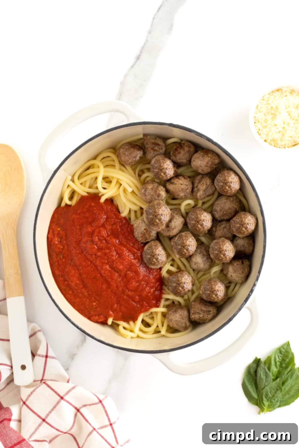 A large white dutch oven with spaghetti noodles, red sauce and meatballs.