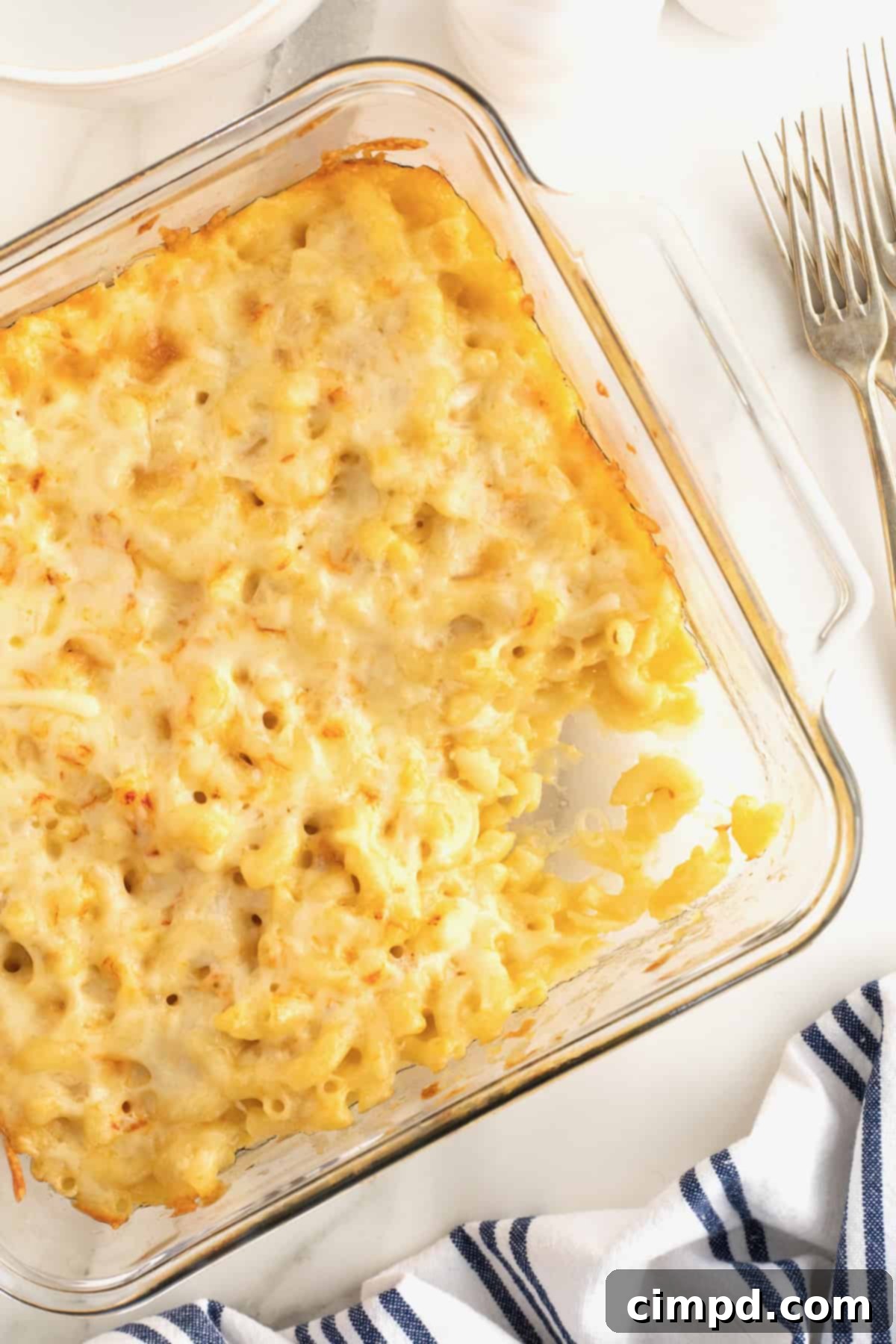 Creamy Muenster Mac and Cheese 2 A square glass dish filled with golden-brown Muenster Mac and Cheese, with a portion removed to reveal its creamy interior.