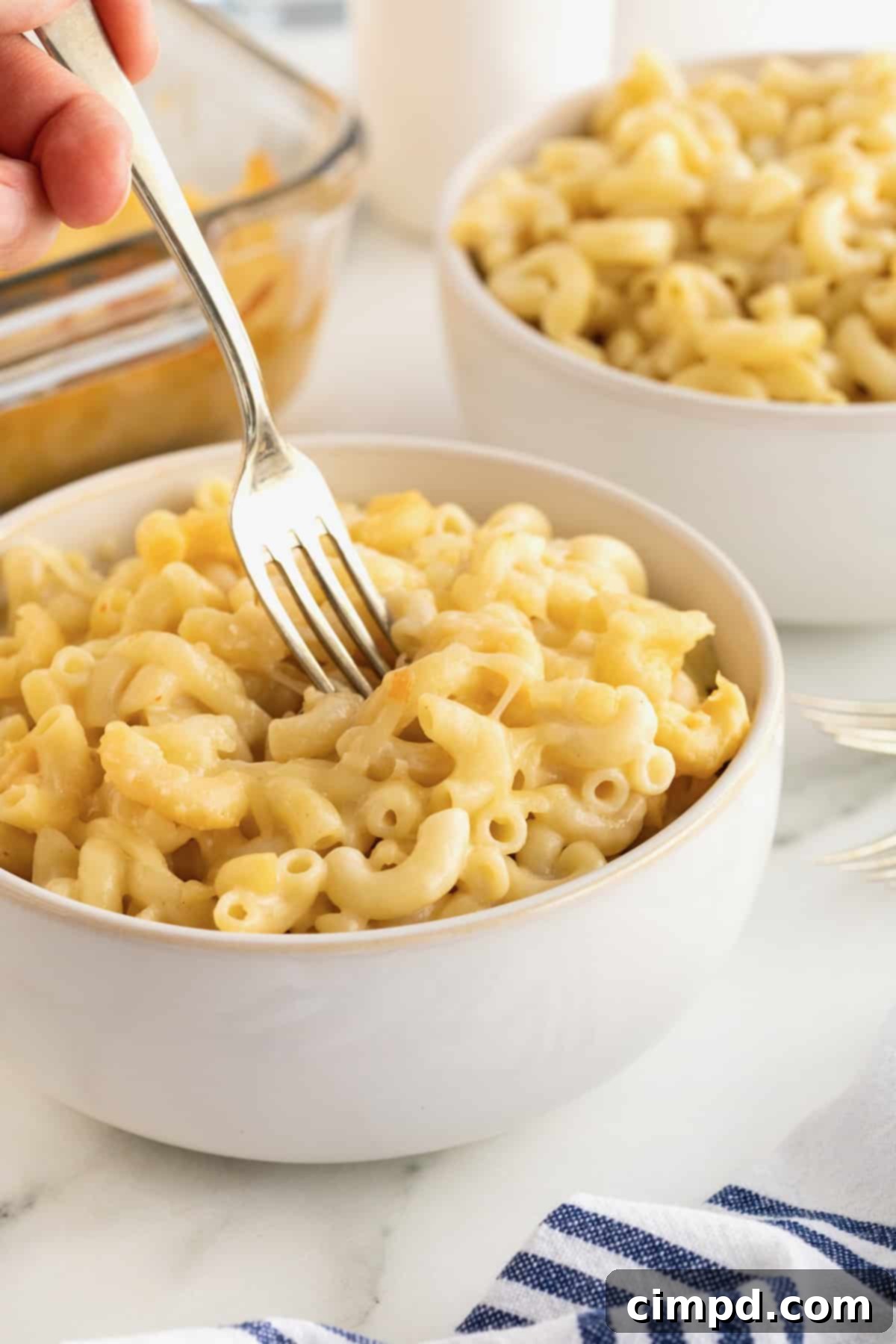 Creamy Muenster Mac and Cheese 4 A white ceramic bowl brimming with Muenster Mac and Cheese, a metal fork poised within its cheesy depths.