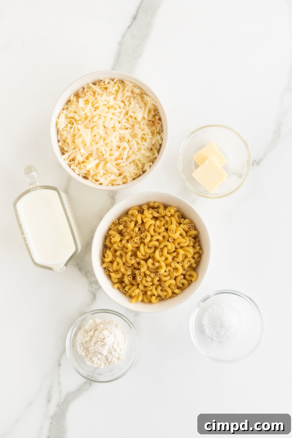 Creamy Muenster Mac and Cheese 5 A neatly arranged collection of ingredients for Muenster Mac and Cheese in small glass dishes on a white marble counter.