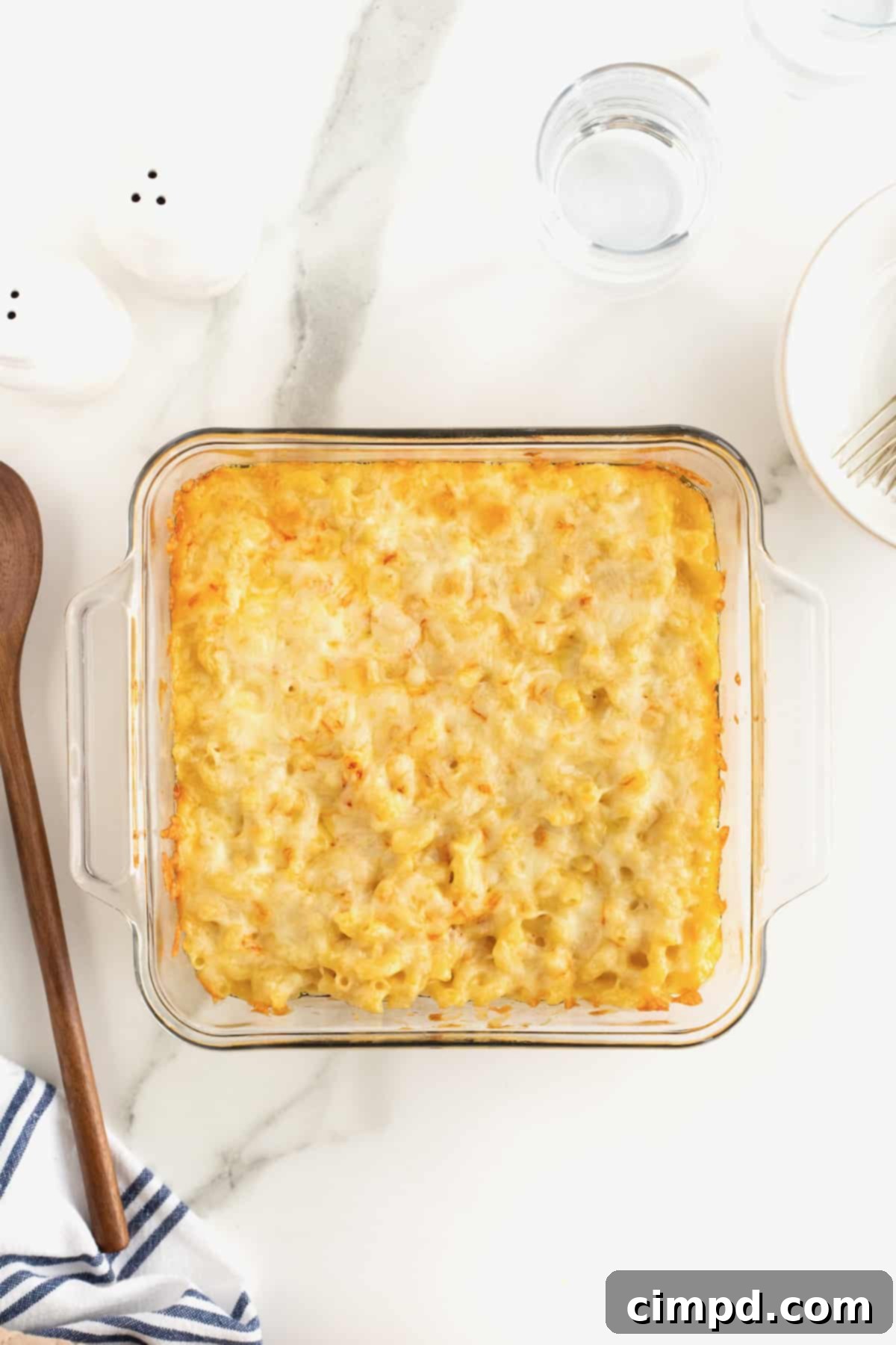 Creamy Muenster Mac and Cheese 10 A perfectly baked square glass dish of Muenster Mac and Cheese, with a golden-brown, bubbly top and a wooden spoon resting beside it.