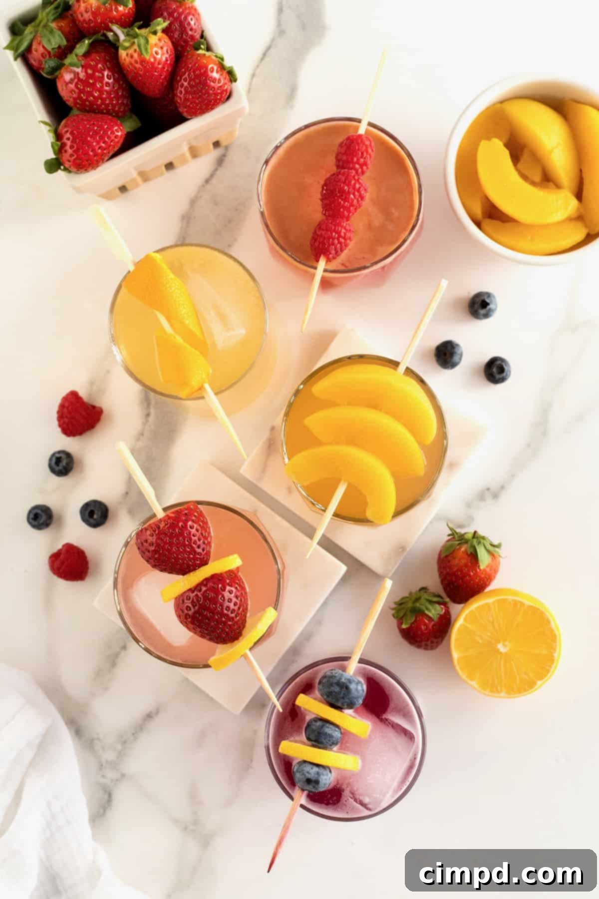 An aerial view of several vibrant 4-Ingredient Jam Cocktails, artfully arranged amidst scattered fresh fruits that highlight their flavors.