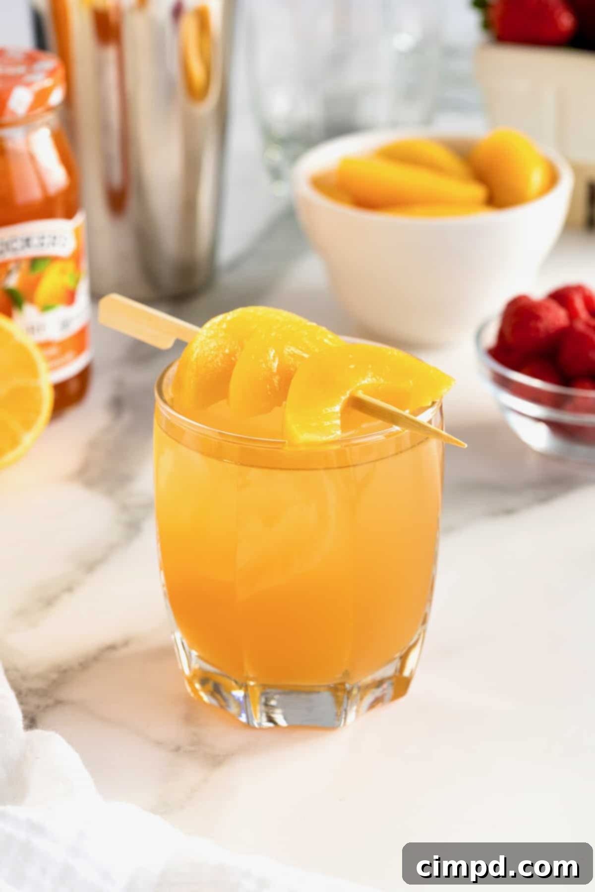 A beautiful peach jam cocktail, garnished with fresh peach slices on a wooden food pick, highlighting its natural and inviting aesthetic.