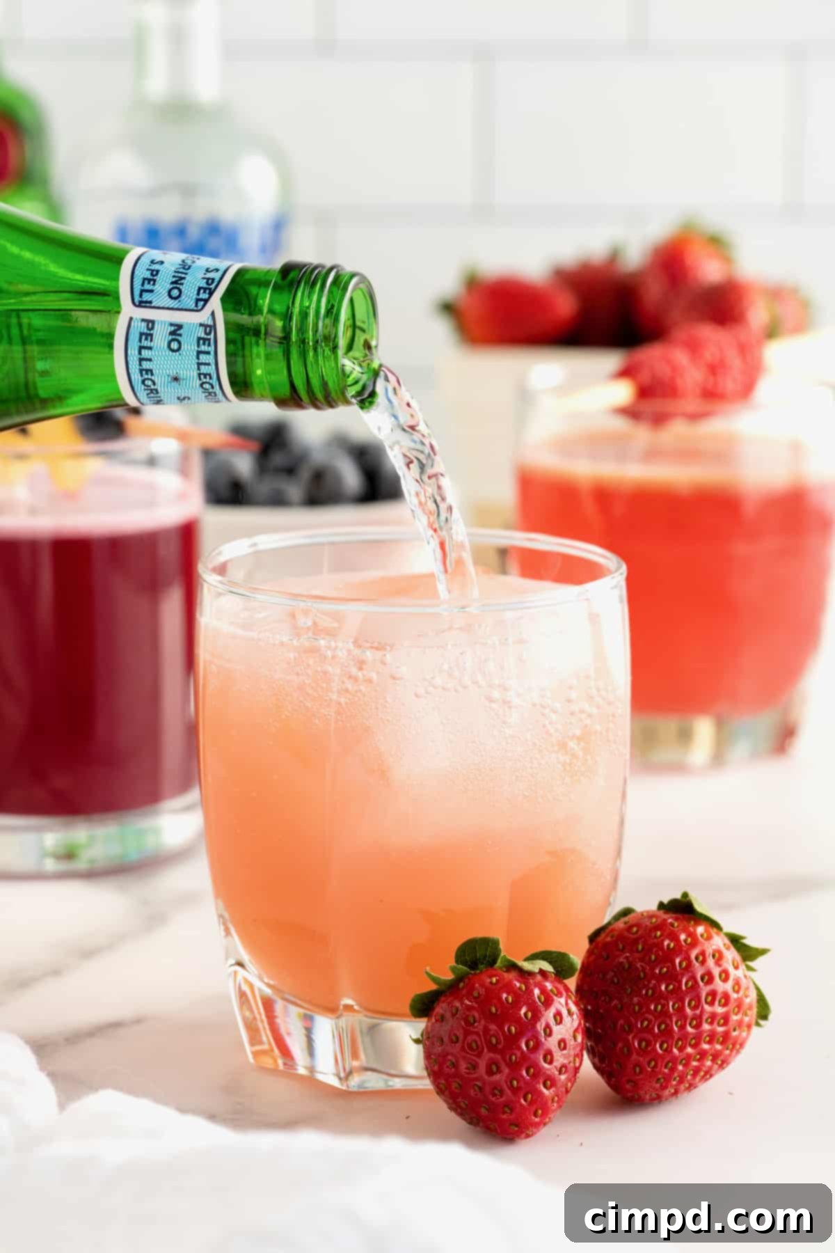 Sparkling water being carefully poured from a green glass bottle into a vibrant pink cocktail, creating a refreshing fizz.