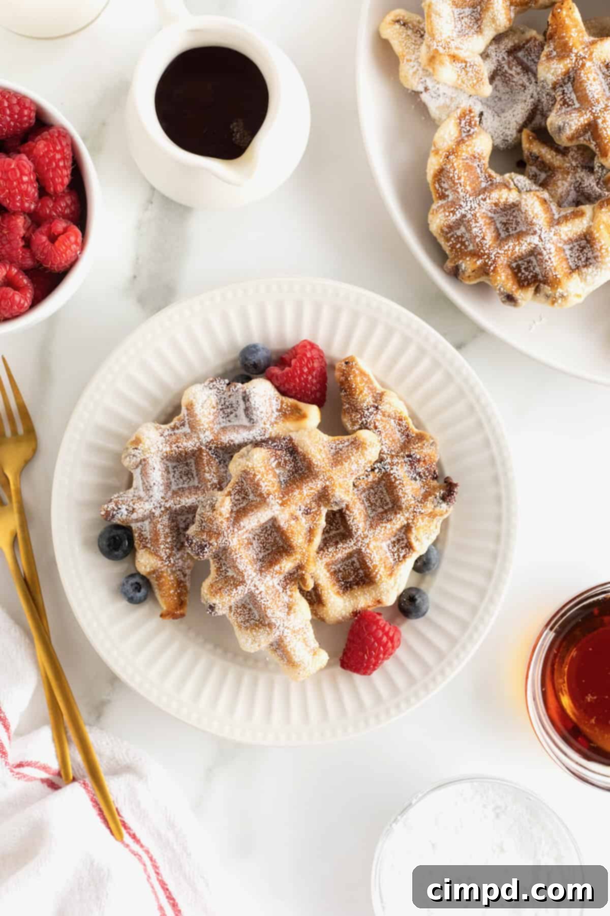 A large white fluted plate with two waffle-textured pastries topped with blueberries and strawberries.