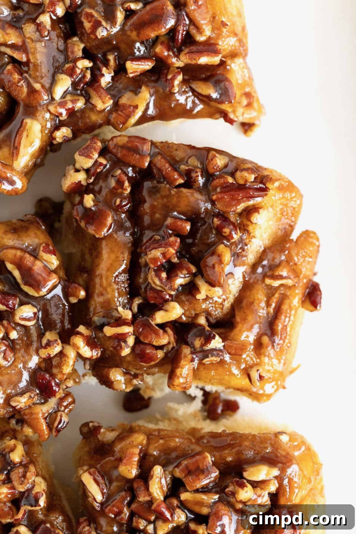 Three sticky buns with chopped pecans on them on a white surface.