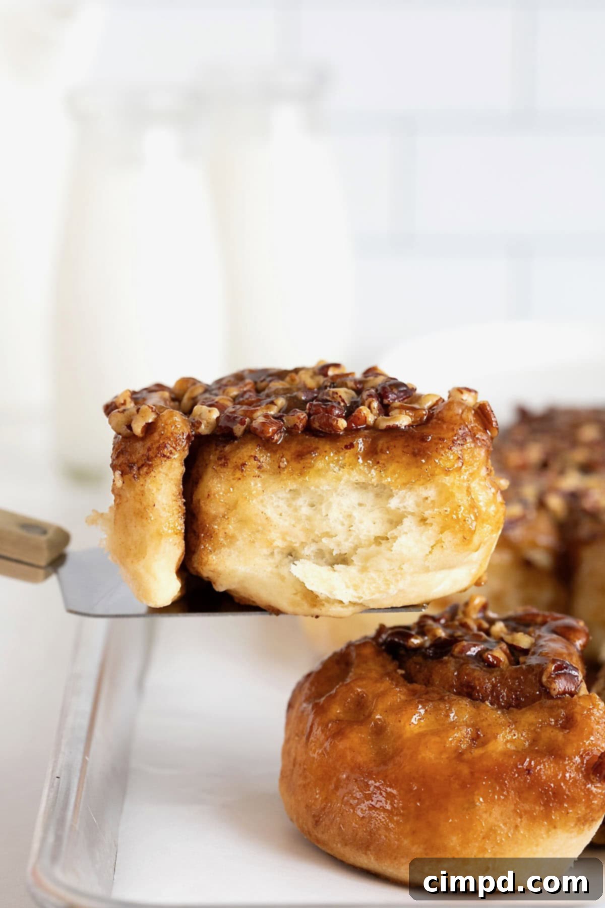 A sticky bun on a spatula being lifted from a parchment lined aluminum baking sheet of sticky buns.