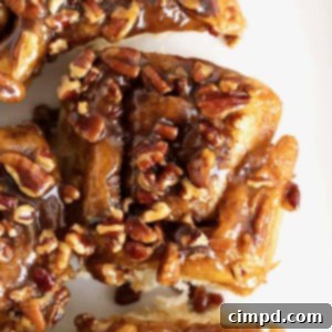 Three sticky buns with chopped pecans on them on a white surface.