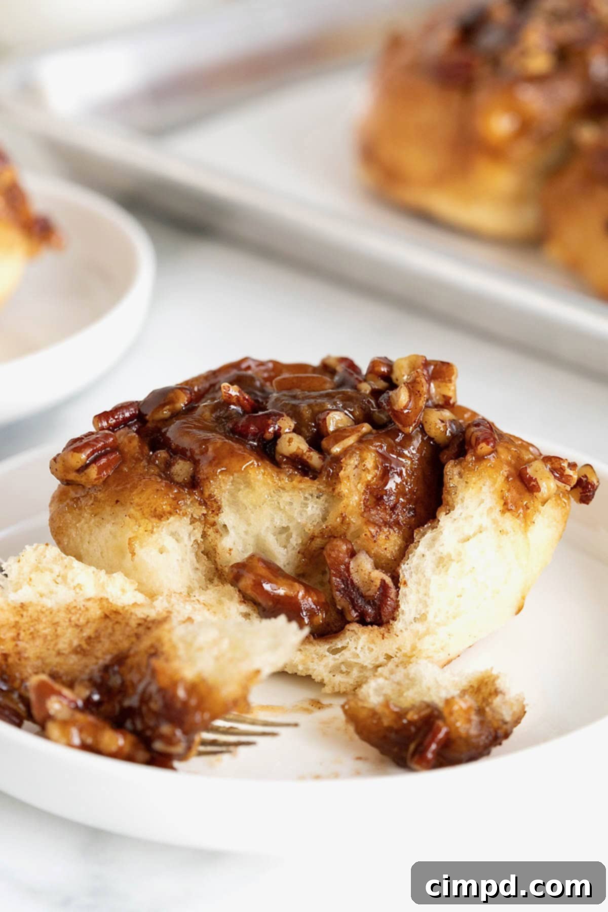 A sticky bun on a white rimmed plate with a fork.