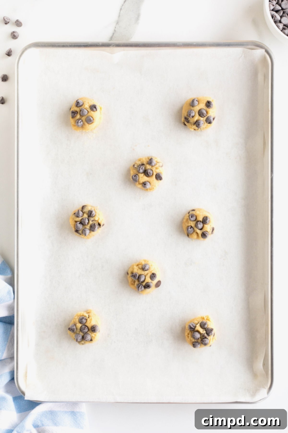 The Ultimate Chocolate Chip Cookies 9 Eight perfectly portioned chocolate chip cookie dough balls are neatly arranged on a parchment-lined baking sheet, spaced for optimal baking.