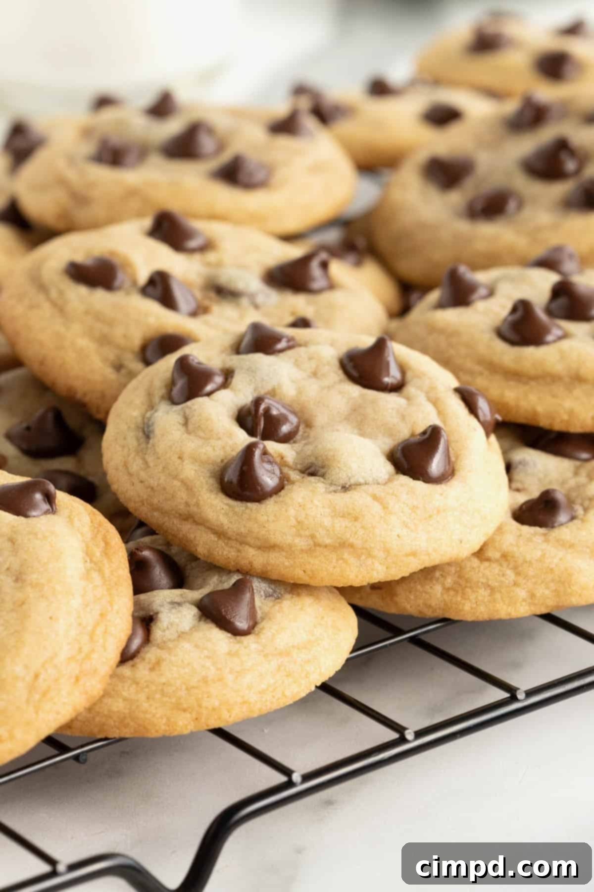 The Ultimate Chocolate Chip Cookies 4 A dark metal cooling rack holds a generous batch of classic chocolate chip cookies, their golden-brown hues and visible chocolate chips inviting a taste.