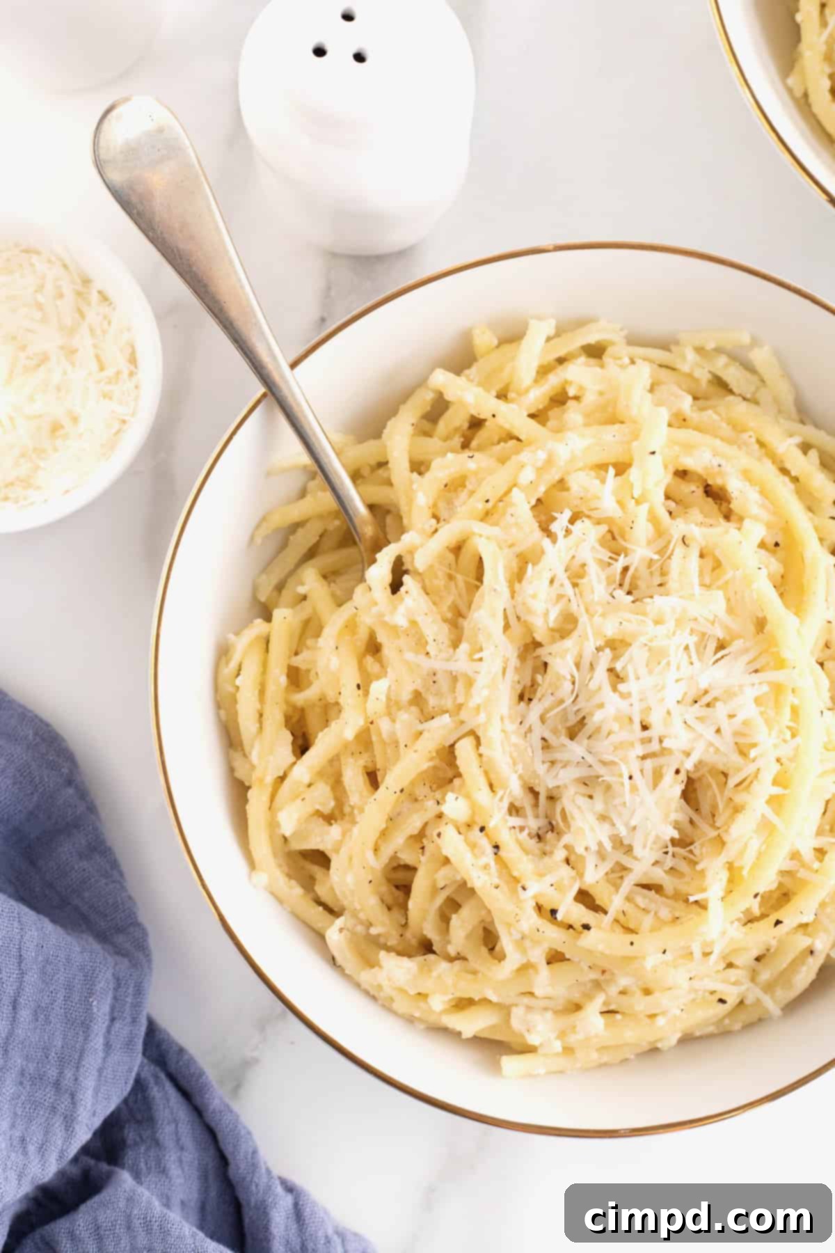 A large white, gold-rimmed serving bowl of Cacio e Pepe, showcasing its creamy texture and freshly ground black pepper.