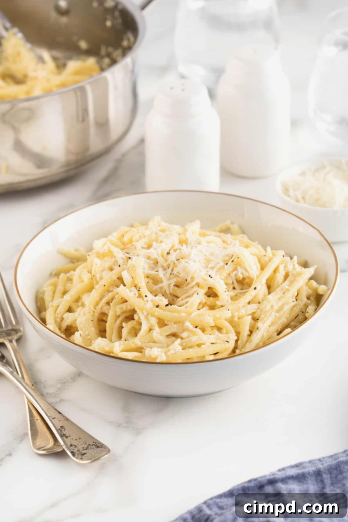 A large white, gold-rimmed serving bowl of Cacio e Pepe, showcasing its rich, golden hue.