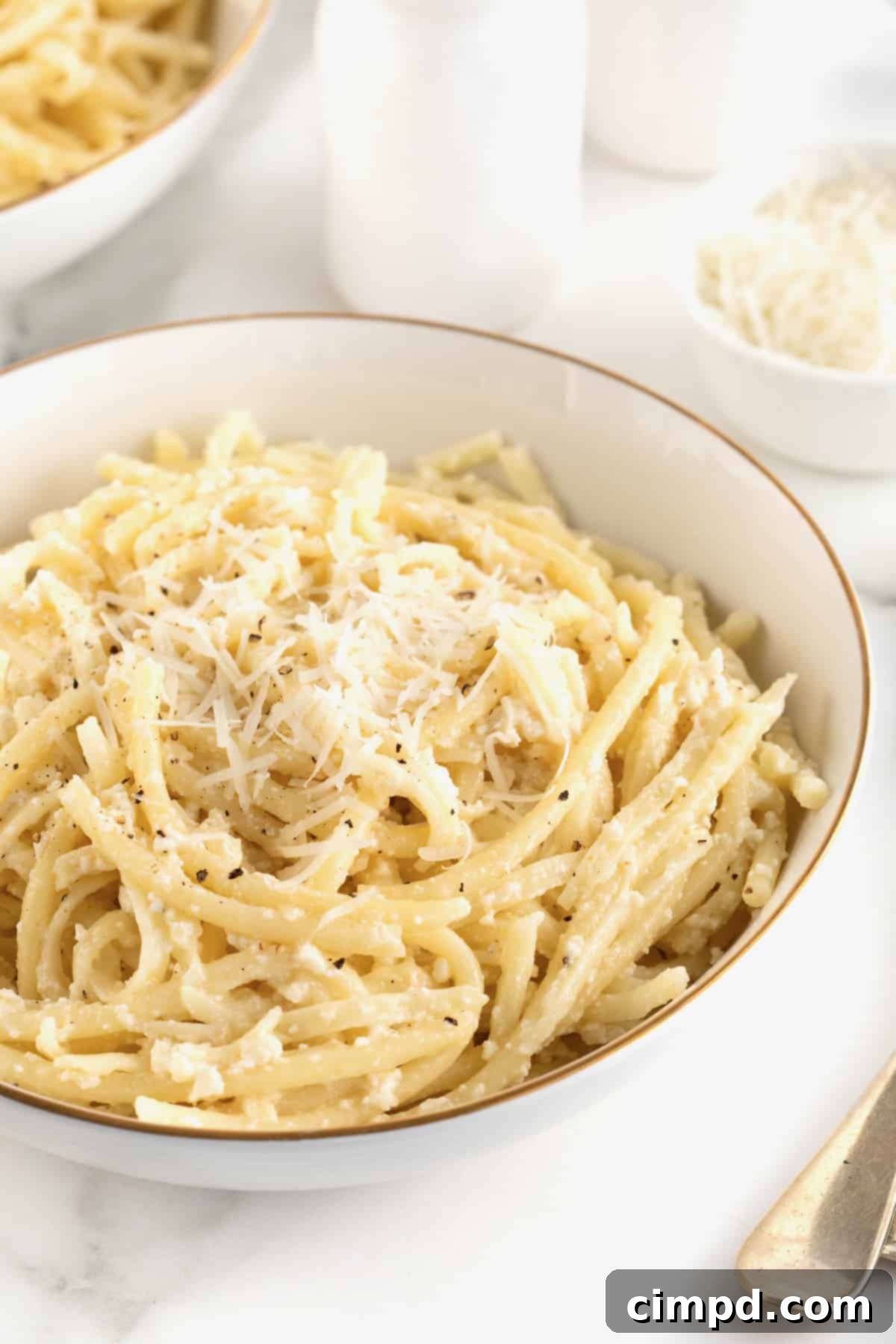 A large white, gold-rimmed serving bowl of Cacio e Pepe, freshly prepared and garnished.