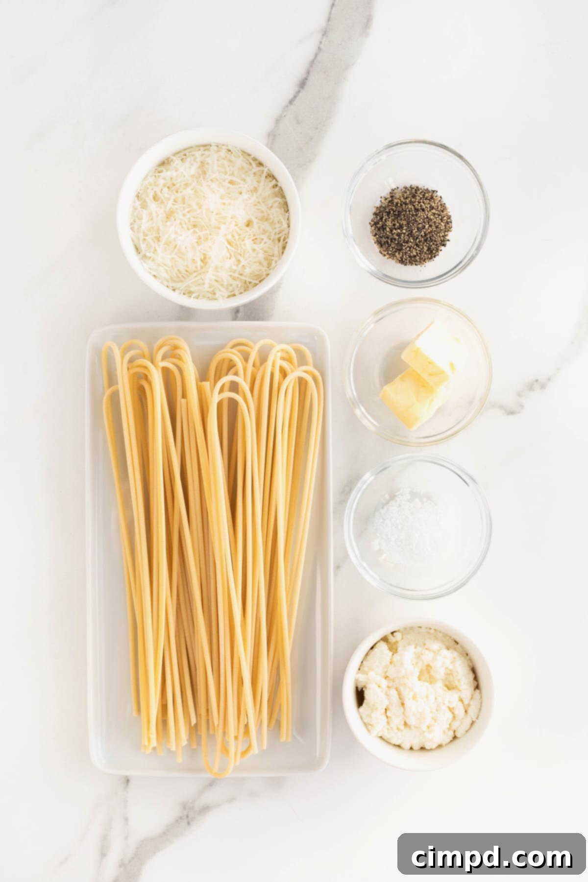 Ingredients for Cacio e Pepe laid out in small dishes on a white marble counter: pasta, butter, ricotta, Pecorino Romano, black pepper, and salt.