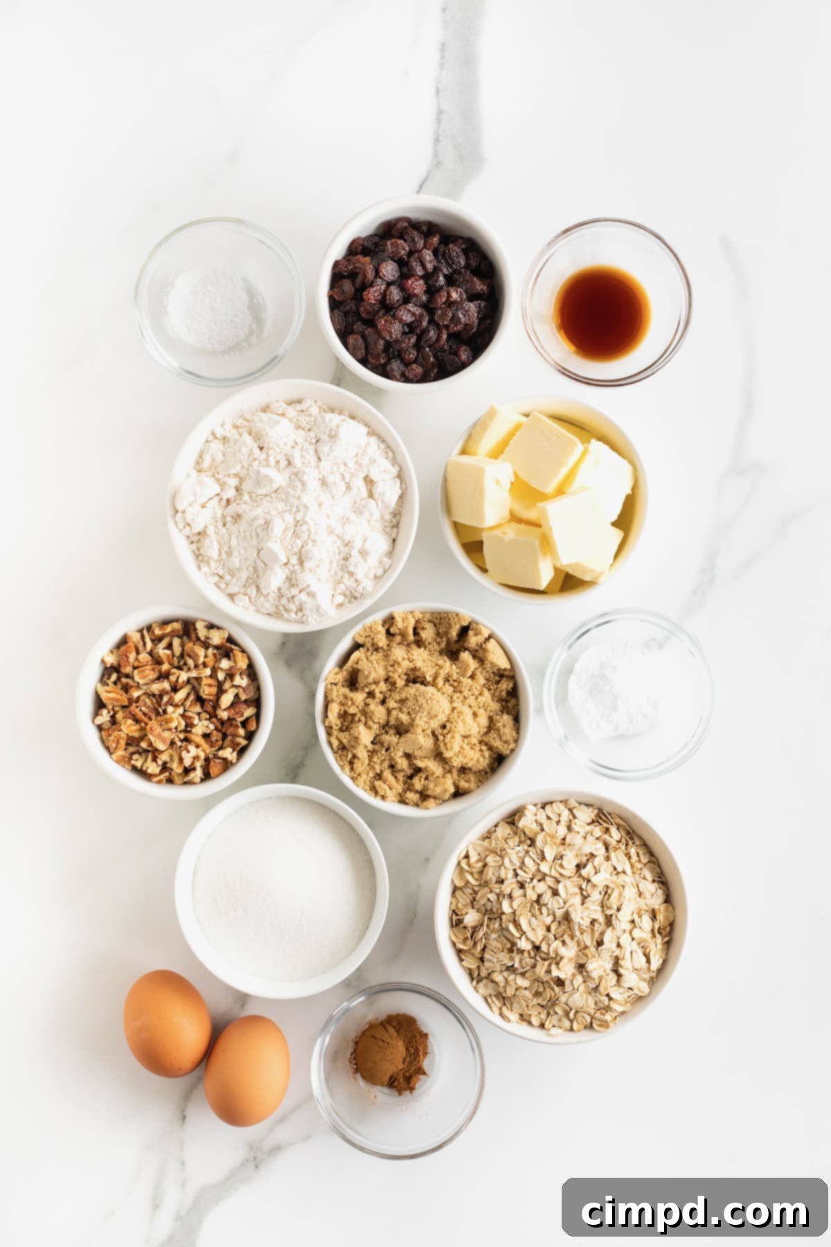 Pecan Oatmeal Raisin Cookies 6 Various ingredients for oatmeal raisin pecan cookies meticulously arranged in small glass dishes on a pristine white marble counter.