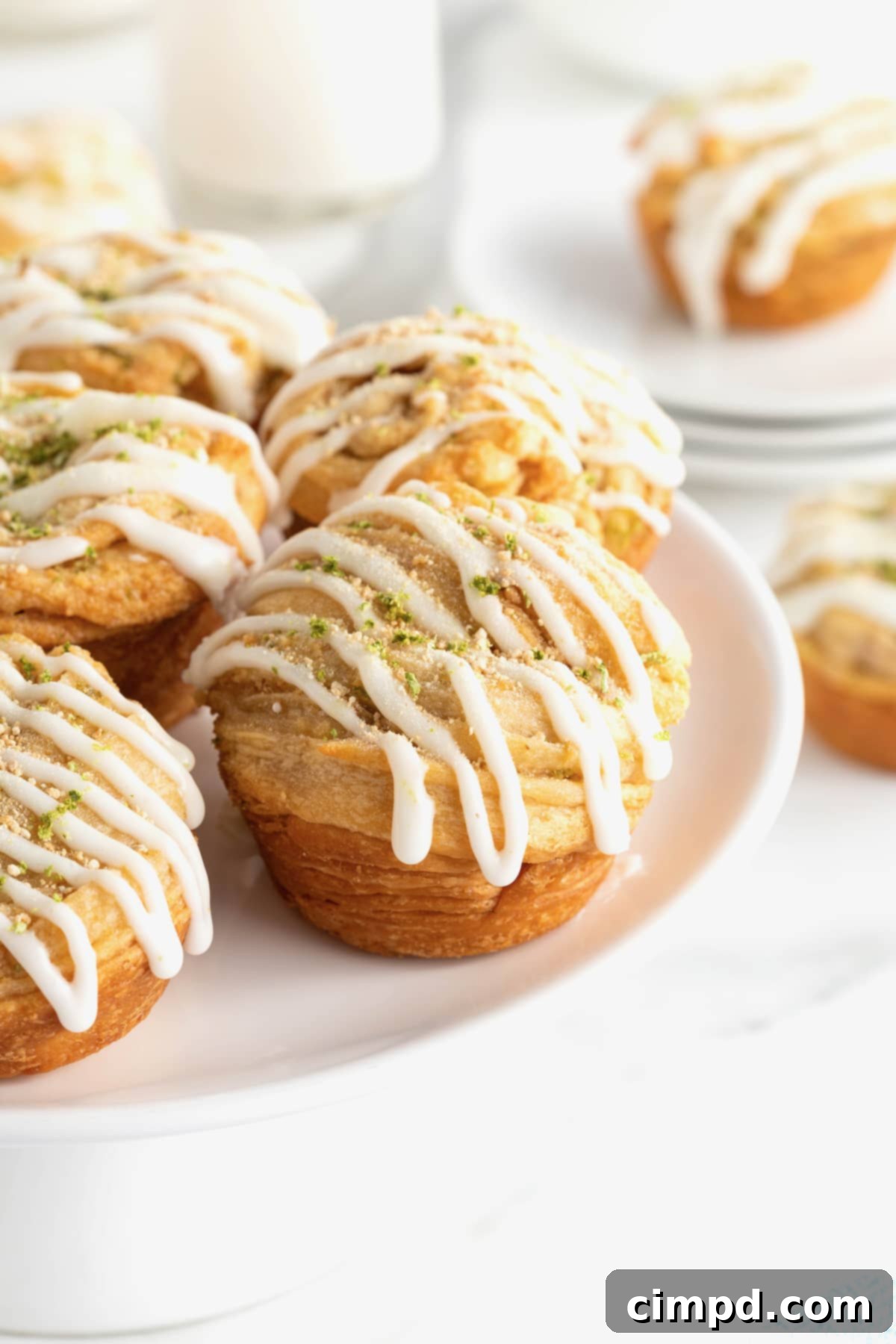 Five Key Lime Cruffins beautifully arranged on a large white round serving platter, showcasing their golden-brown layers and creamy white icing, garnished with lime zest and graham cracker crumbs.
