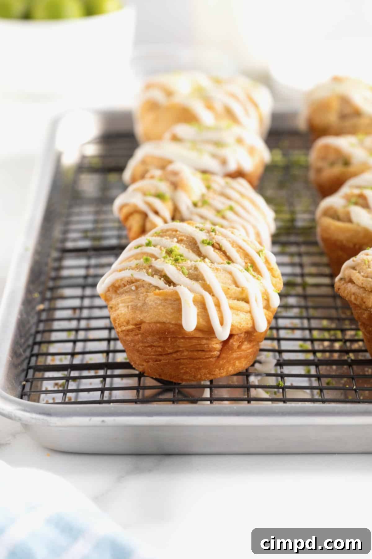 An aluminum baking pan with a wire cooling rack holding Key Lime Cruffins, now beautifully garnished with lime zest and graham cracker crumbs, ready to be served.