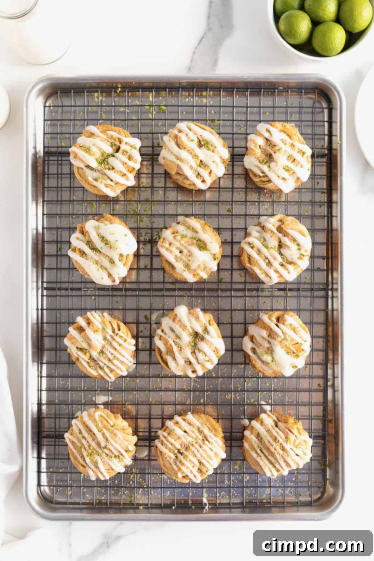 An aluminum baking pan with a wire cooling rack on top, holding a full batch of 12 Key Lime Cruffins, perfectly baked and ready for icing.