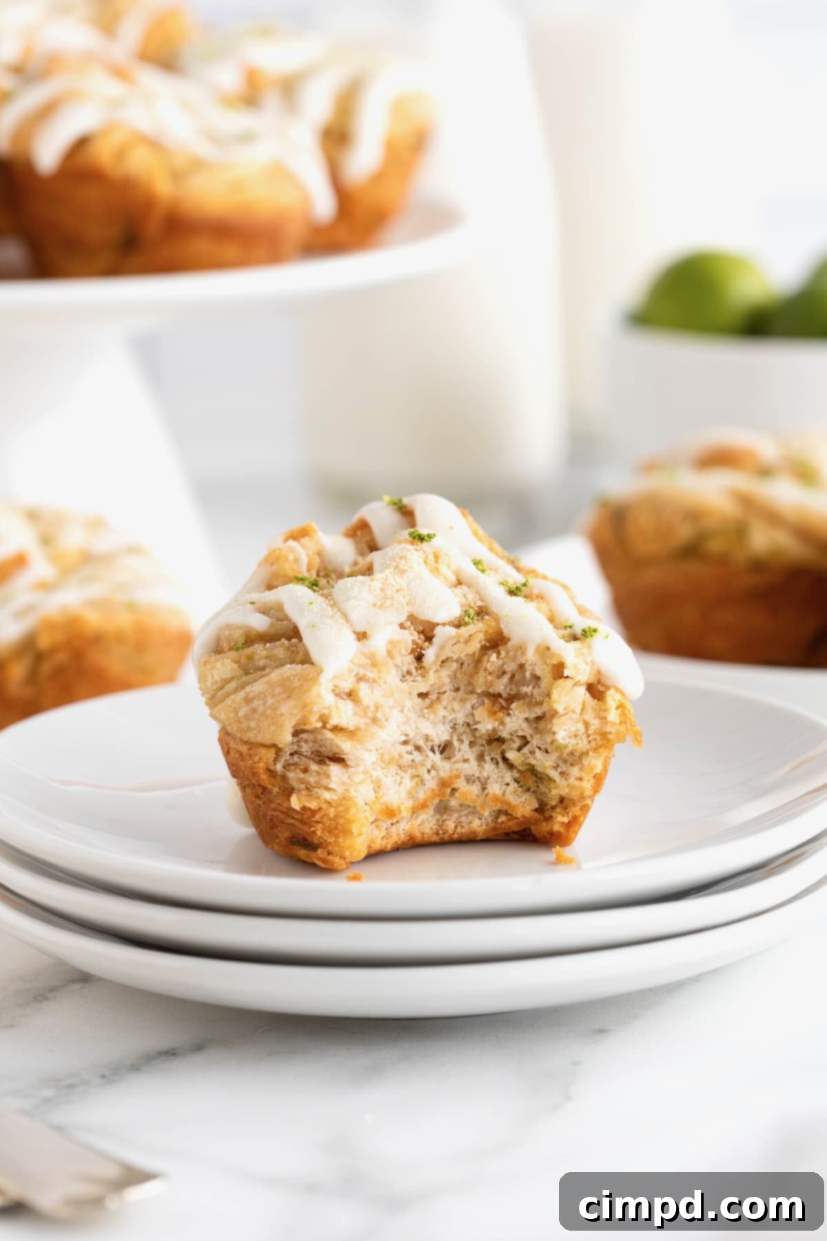 A single Key Lime Cruffin, with a bite taken out, sitting on a small round white plate, revealing its intricate pastry layers and creamy filling.