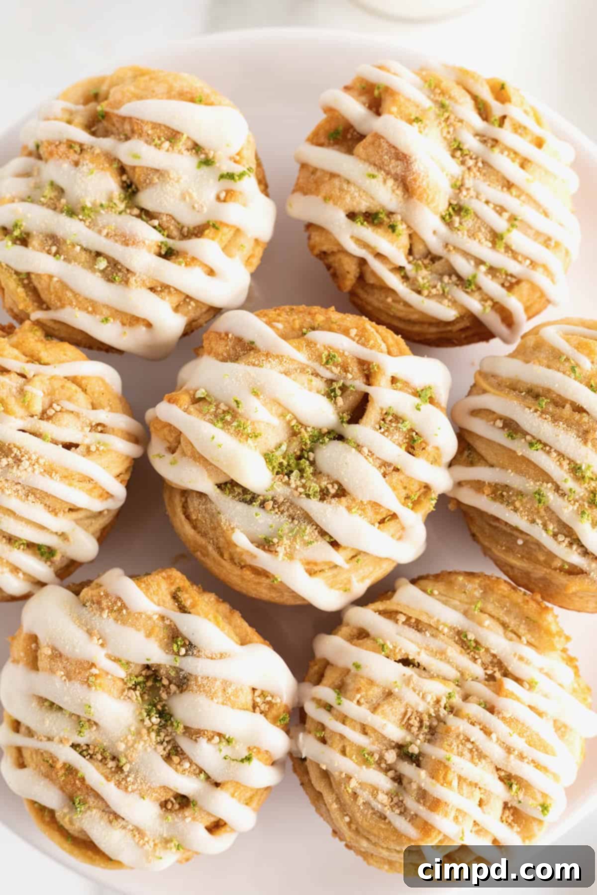 Seven Key Lime Cruffins presented on a large white round serving platter, highlighting their perfect muffin shape, flaky texture, and generous icing.