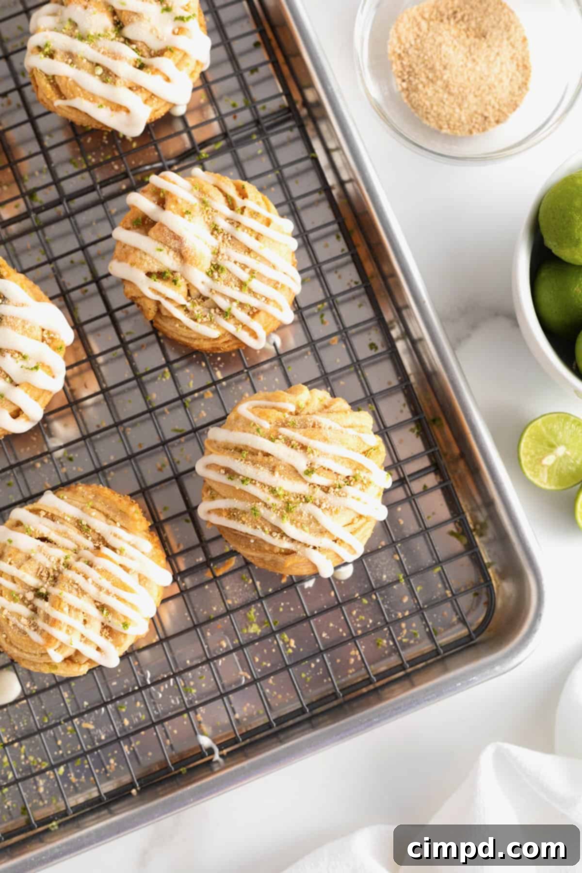 An aluminum baking pan with a wire cooling rack holding four freshly baked Key Lime Cruffins, ready for icing and garnish.