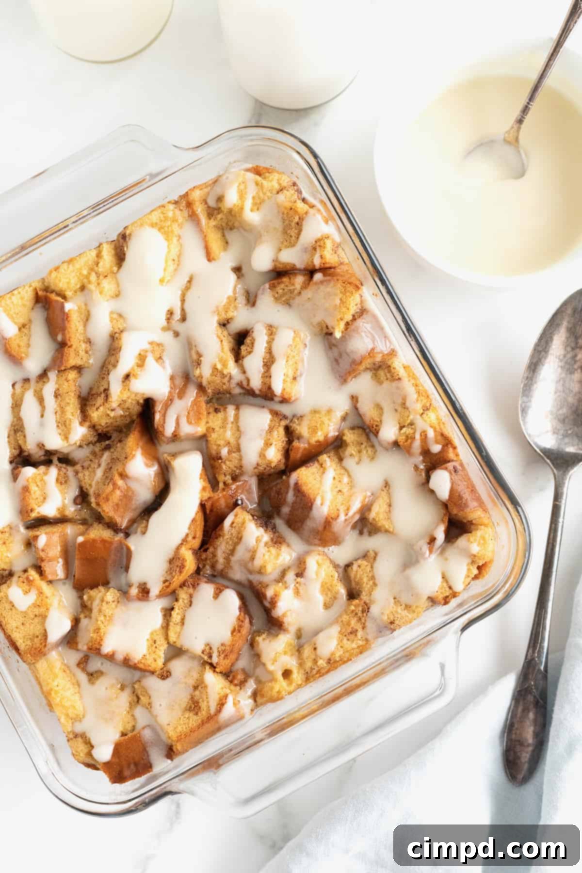 A square glass baking dish of bread pudding with white icing drizzled on top.