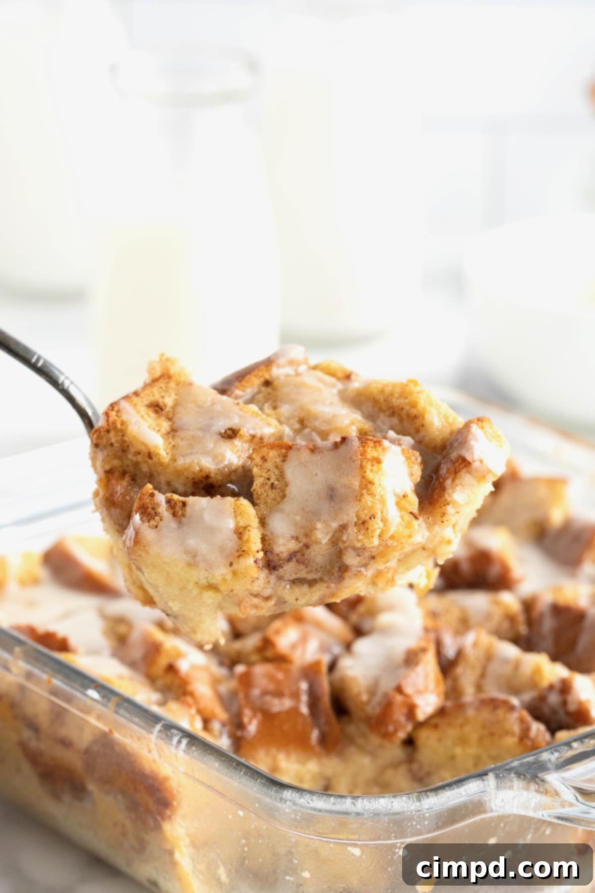 A bite of bread pudding on a fork held over a square glass baking dish of bread pudding. 