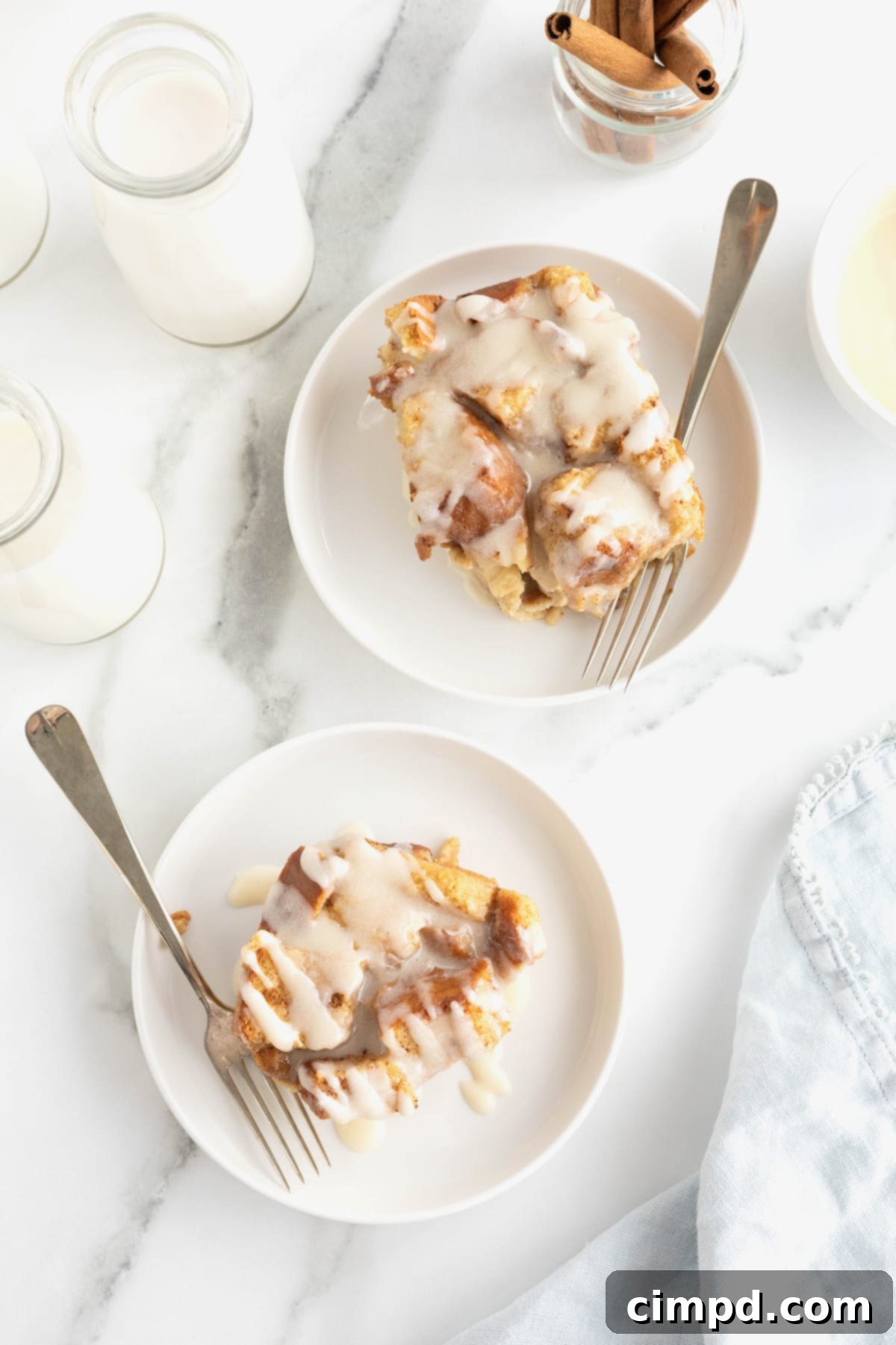 Two white rimmed dessert plates with bread pudding topped with vanilla sauce. 