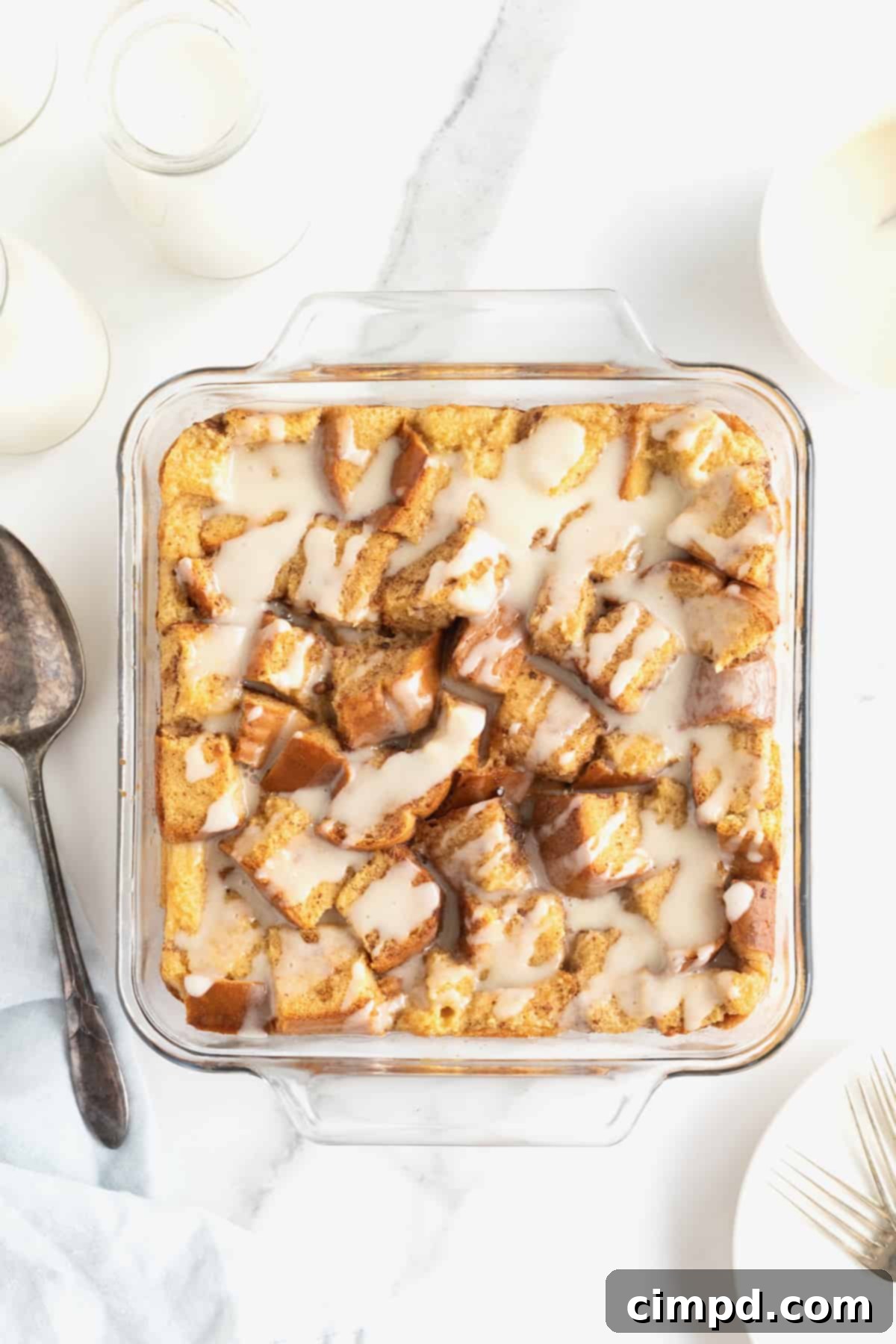 A square glass baking dish of bread pudding with white icing drizzled on top.