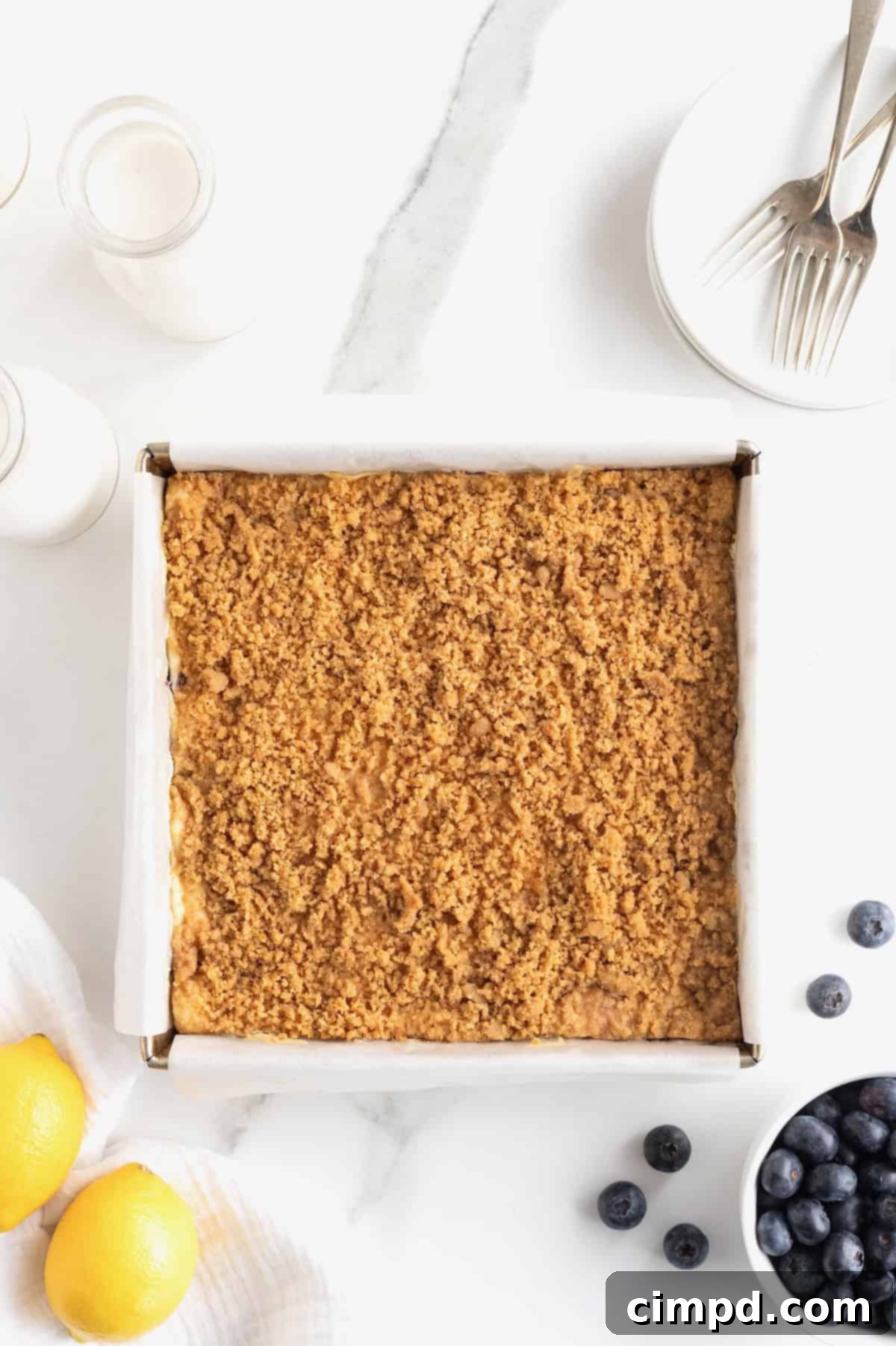 A freshly baked streusel-topped dessert, still in its baking pan lined with parchment paper, cooling after being removed from the oven.