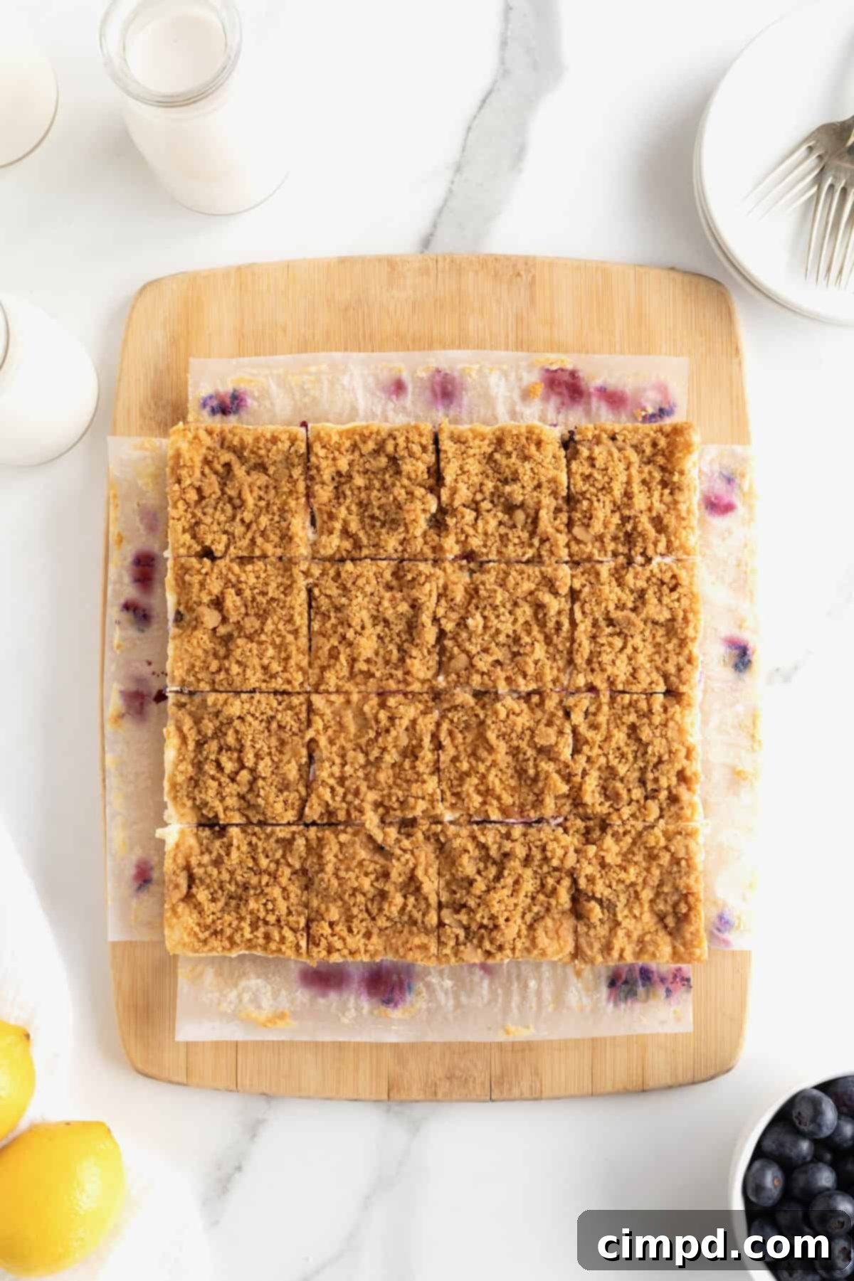 Twelve perfectly cut square lemon blueberry cheesecake bars arranged on a parchment-lined cutting board, ready for serving.