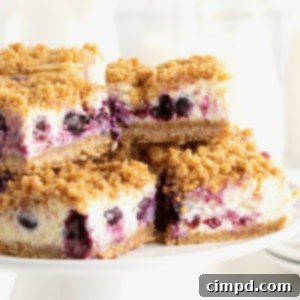 Four lemon blueberry cheesecake bars on a white cake stand.