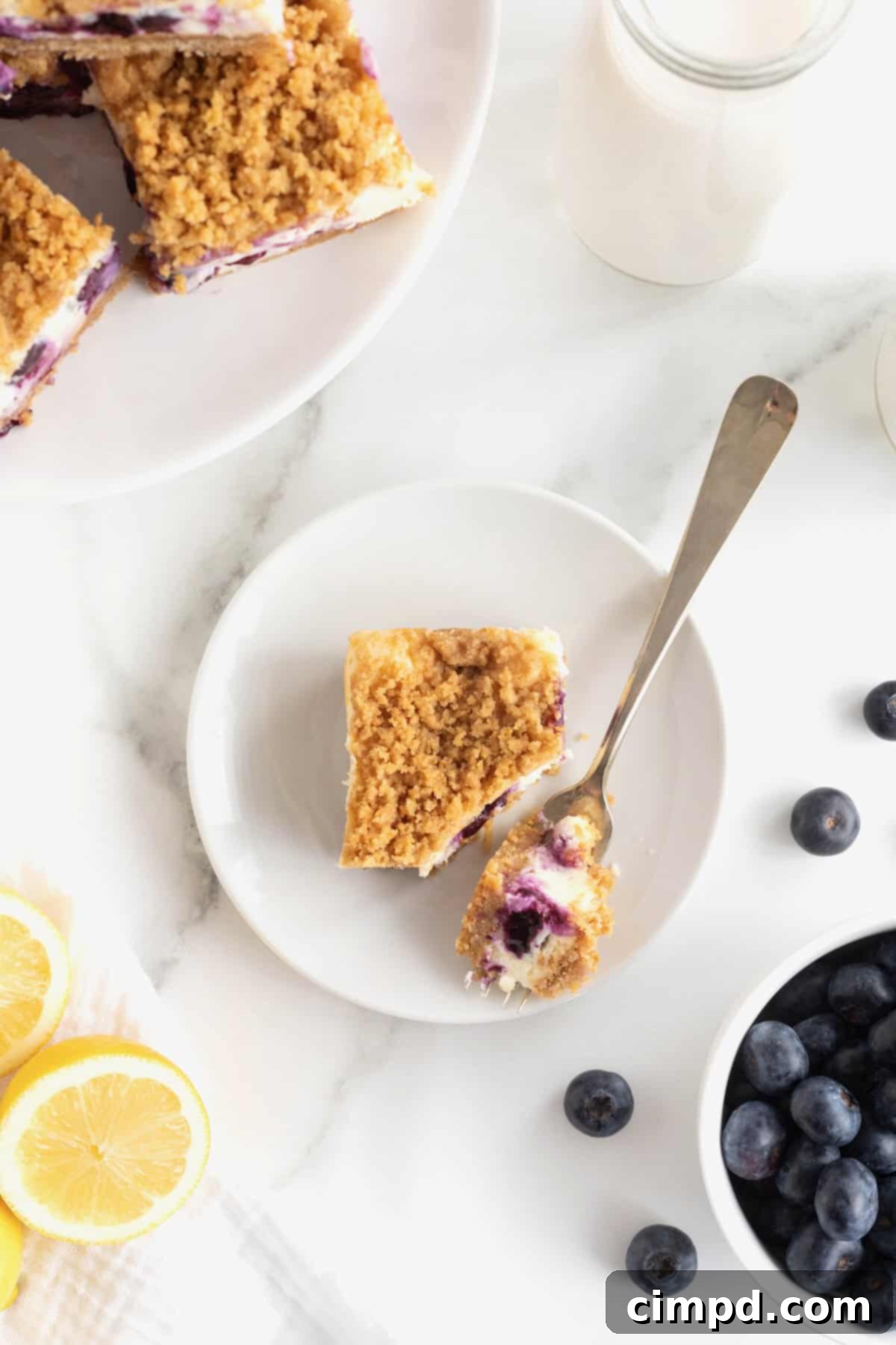 A single lemon blueberry cheesecake bar elegantly presented on a small white dessert plate, with a fork poised to enjoy a bite.