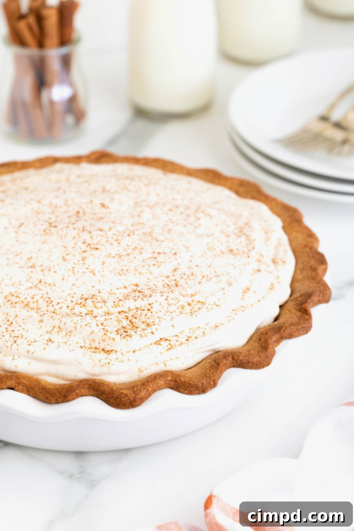 A pumpkin cream pie in a white milk glass pie plate on a white marble counter.