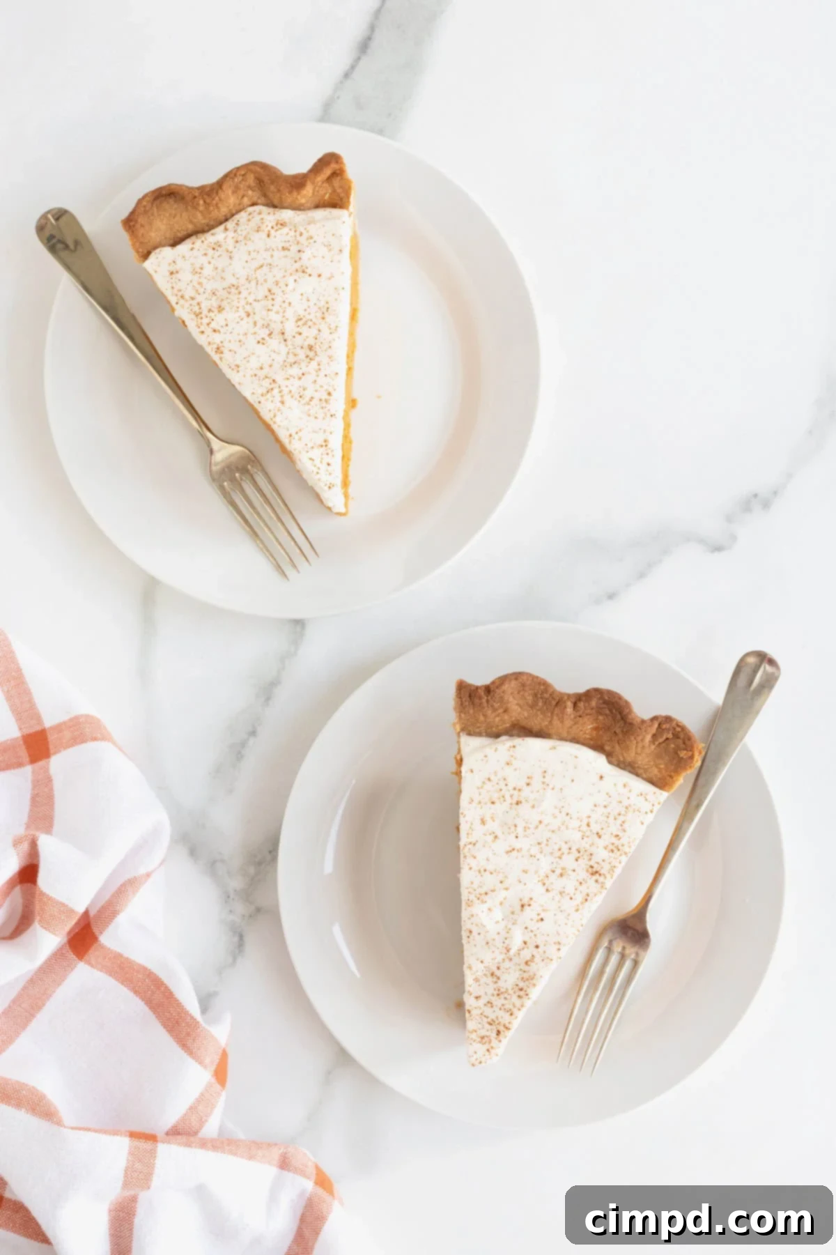 Two slices of pumpkin cream pie on small white dessert plates. There are silver tone forks beside the pie pieces.
